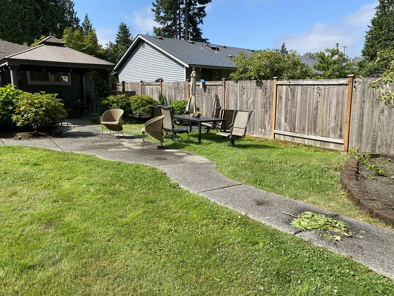Photo of a yard with clover, deck furniture, and a walkway.