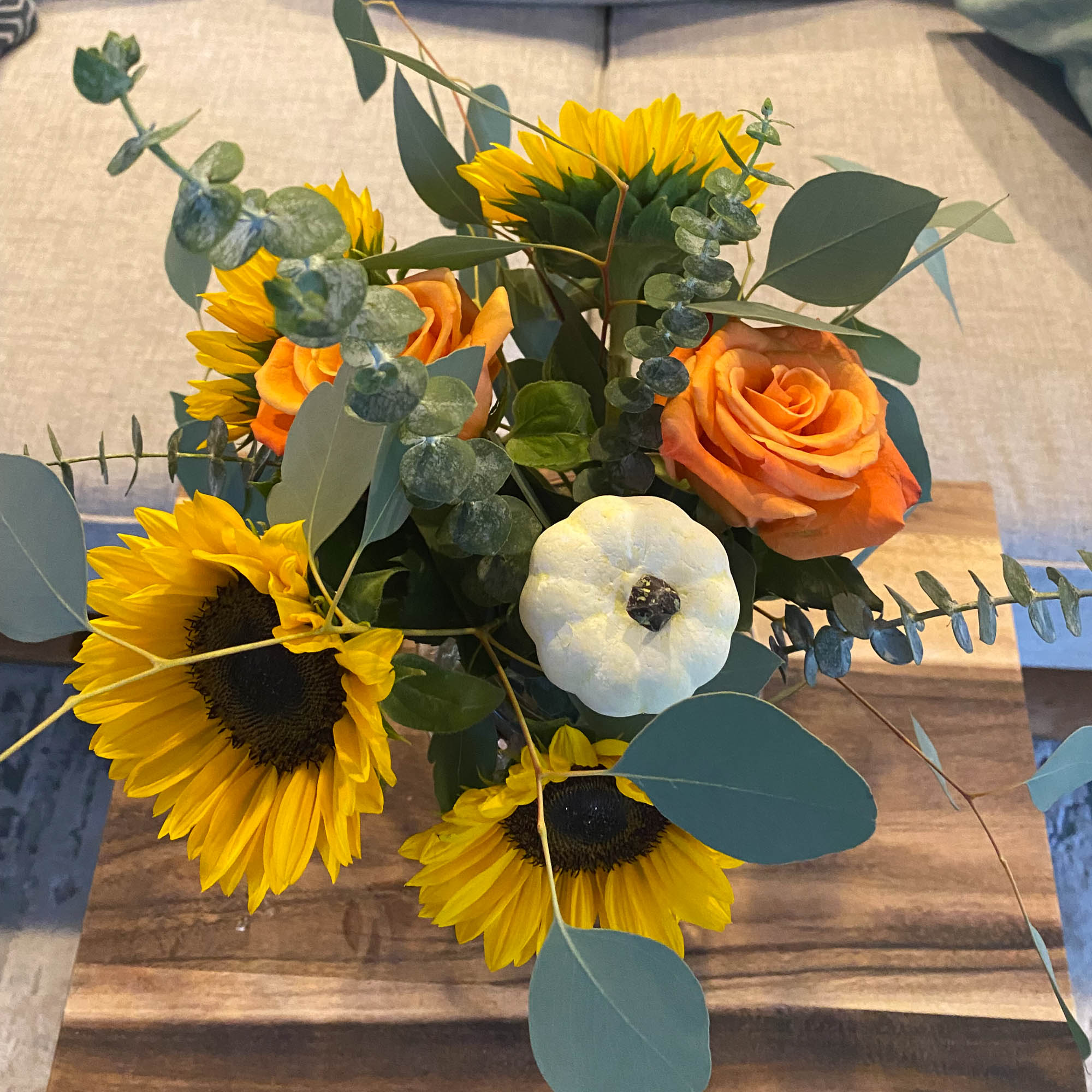 Flower arrangement in a glass vase on a wooden coffee table, with sunflowers and pumpkins.