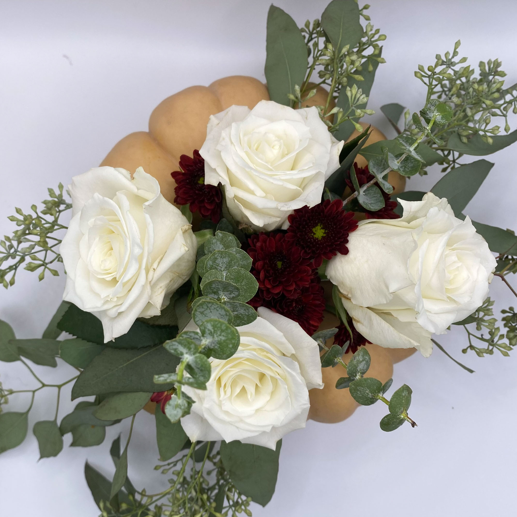Overhead shot of a floral arrangement in a tan pumpkin, with white roses and burgundy flowers.