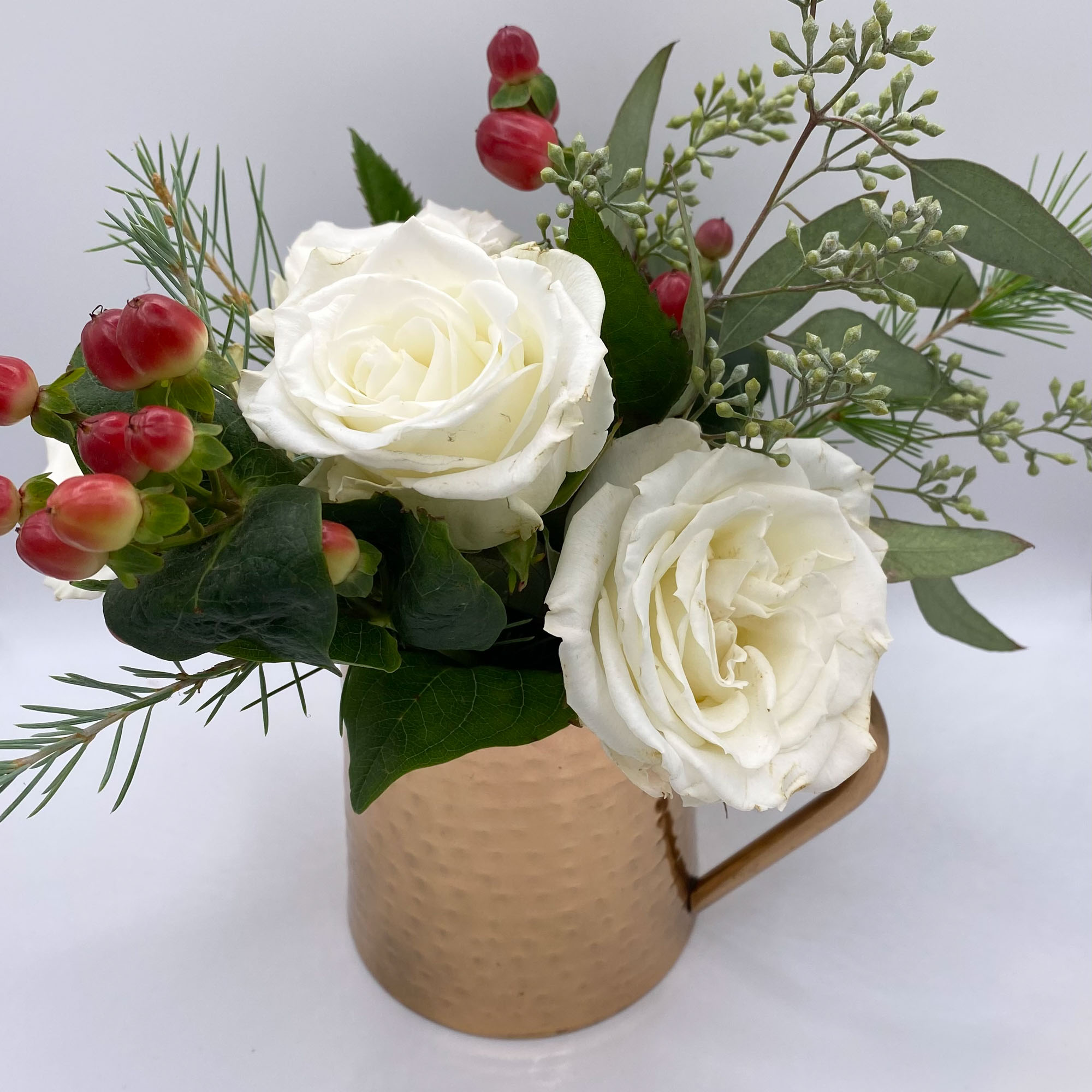 Floral arrangement in a shiny mug, including white roses and other plants.