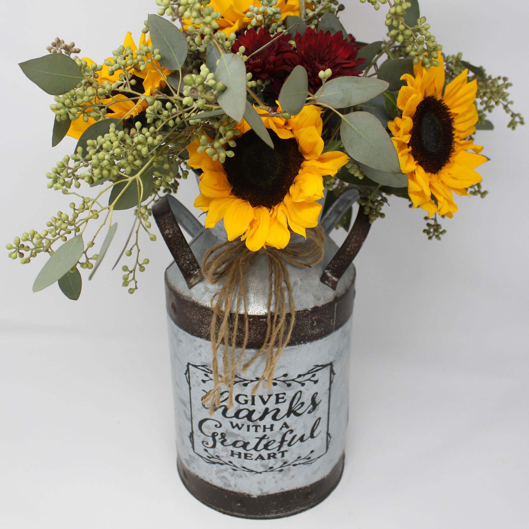 Photo of a floral arrangement with sunflowers and other plants, in a rustic container.