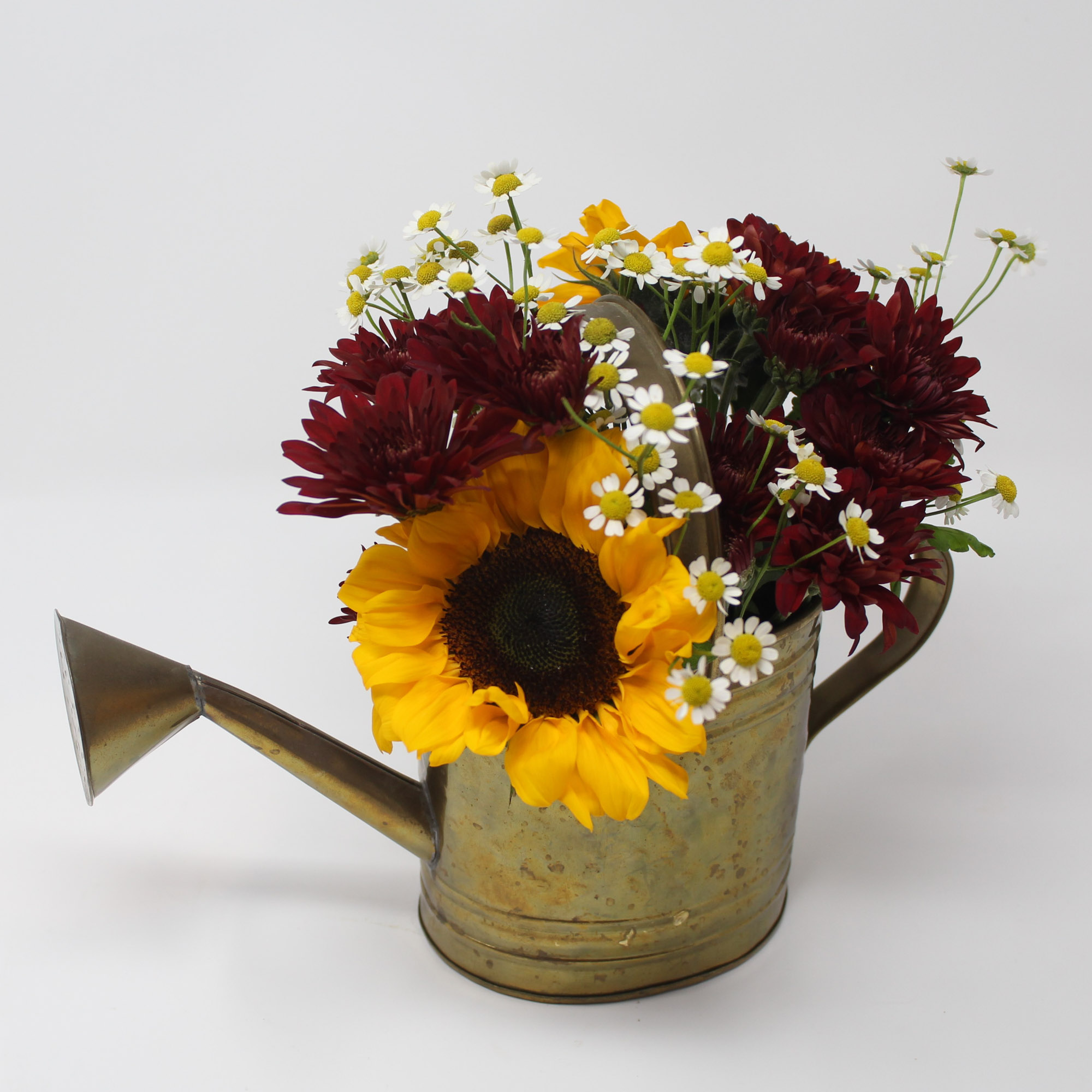 Photo of a floral arrangement with burgundy flowers and sunflowers, in a rustic watering can.