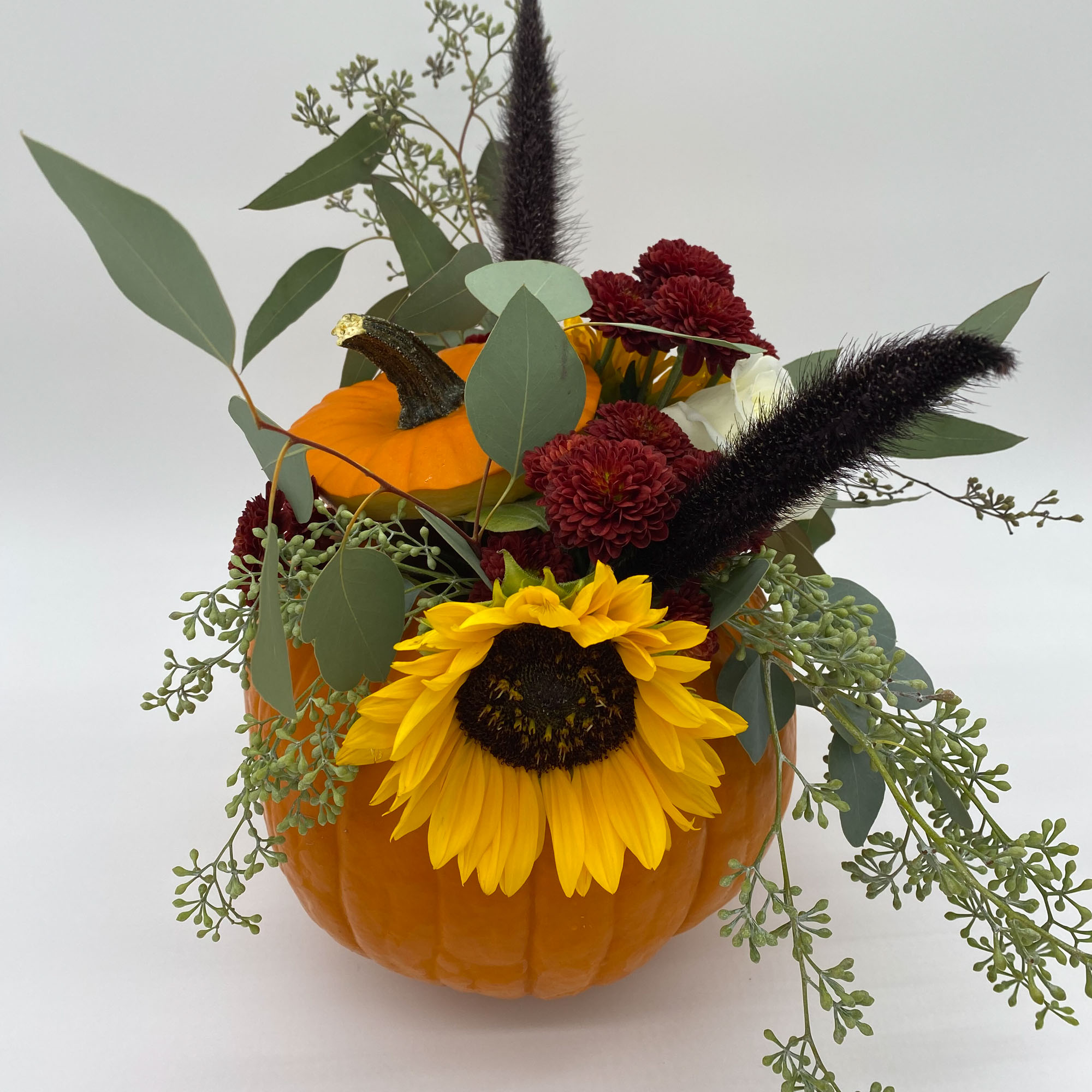 Photo of a floral arrangement with sunflowers and other plants in an orange pumpkin.