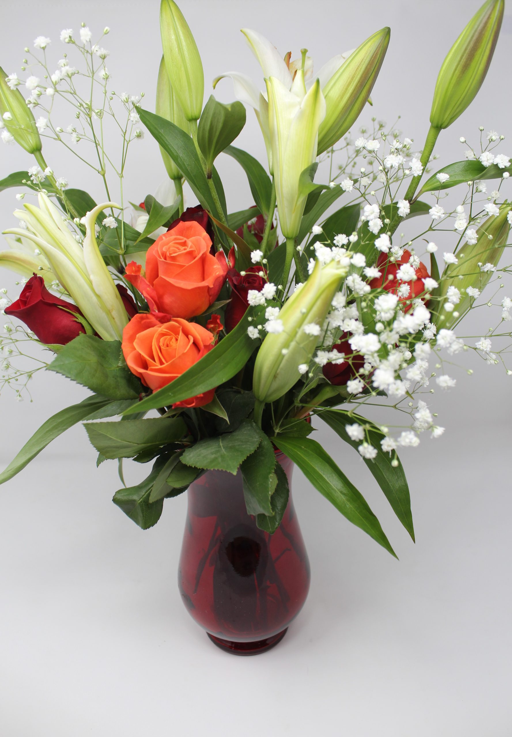 Midshot of a vase with white lilies, orange and red roses, and other flowers.