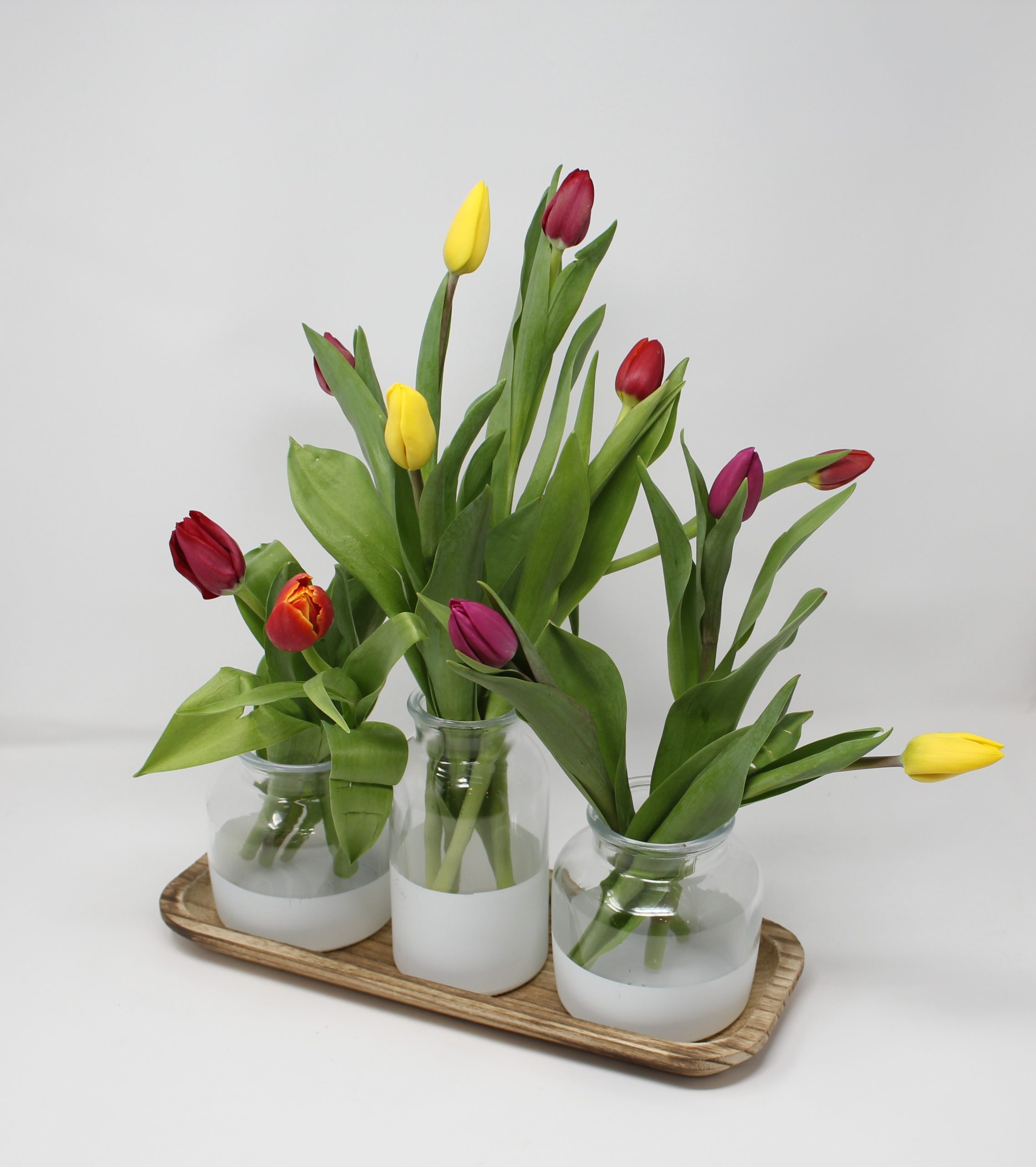 Photo of a wooden tray with three small glass vases with tulips.